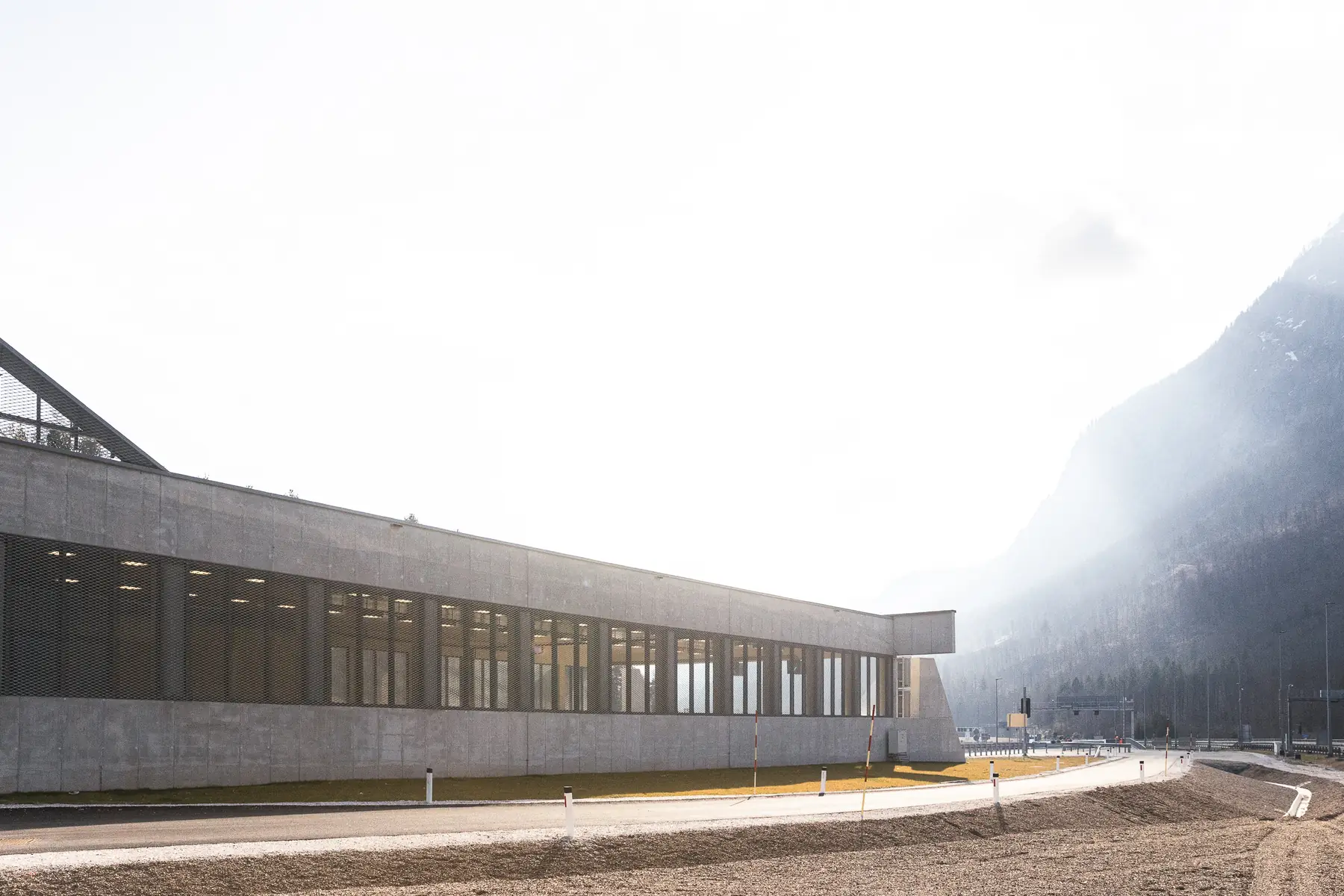 Karavanke tunnel portal area: a long concrete operations building below a fog-covered mountainside